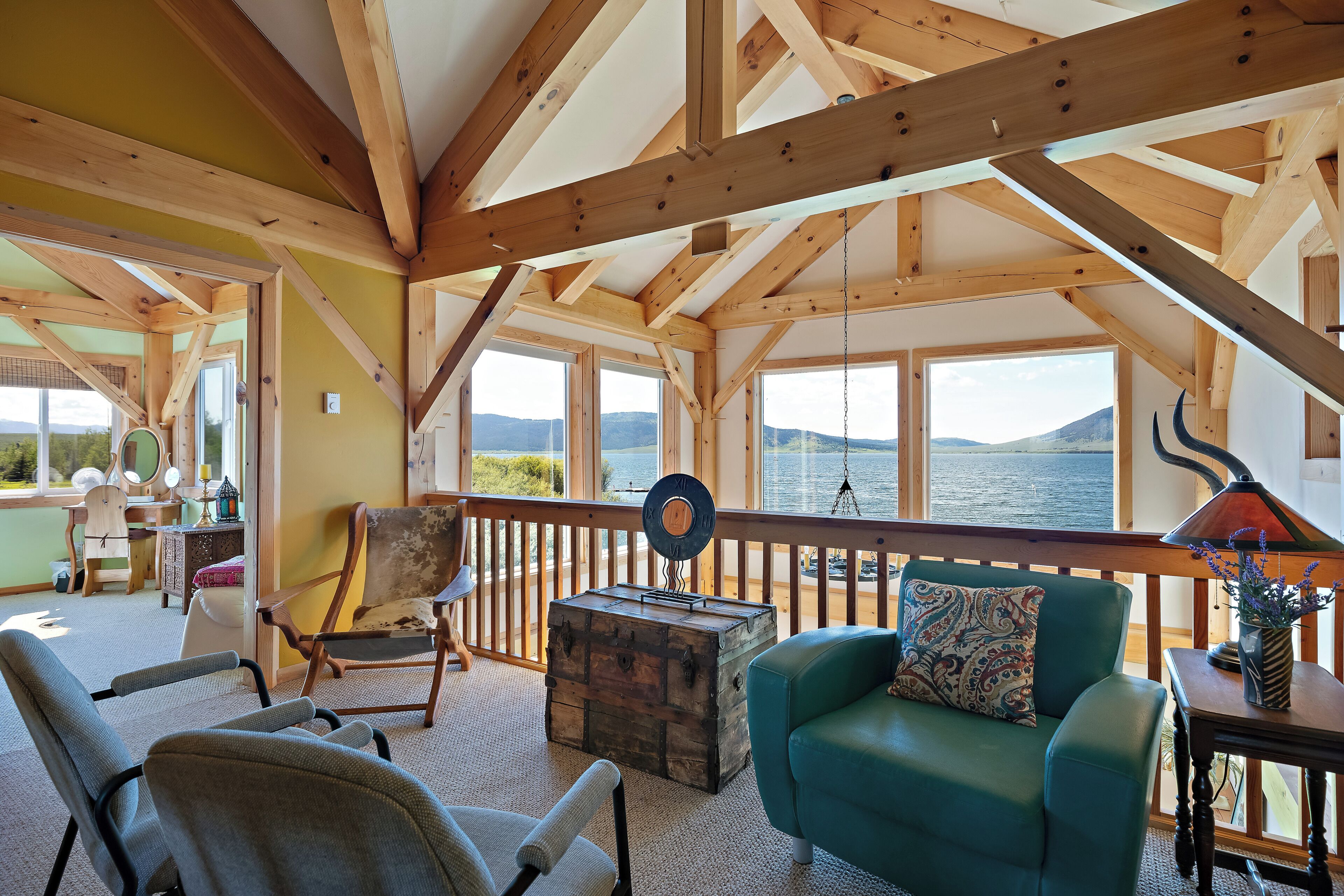 A cozy room with wooden beams, a view of the water, a green sofa, and a wooden chest.