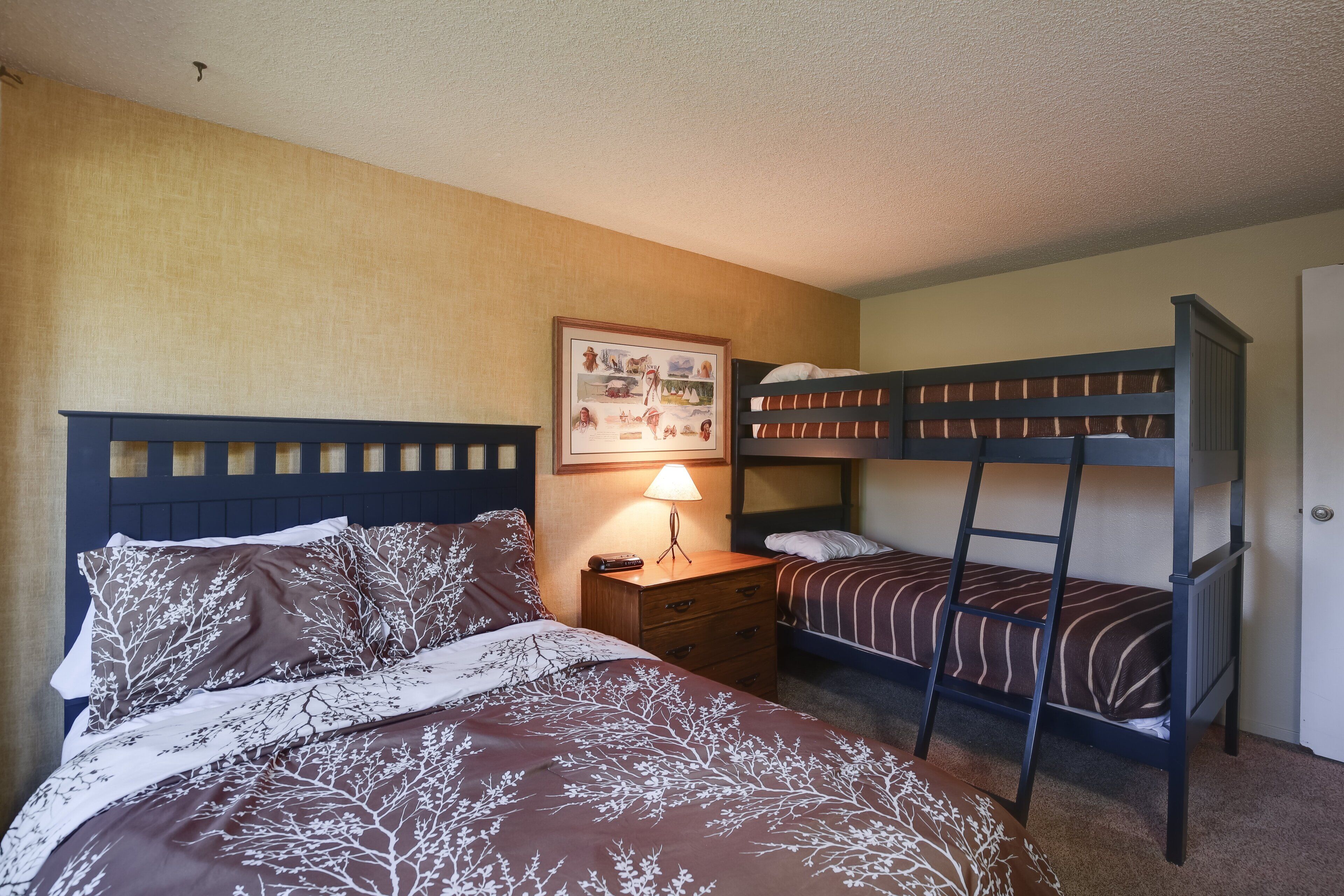 A room with two bunk beds, a nightstand with a lamp, and a framed picture on the wall.