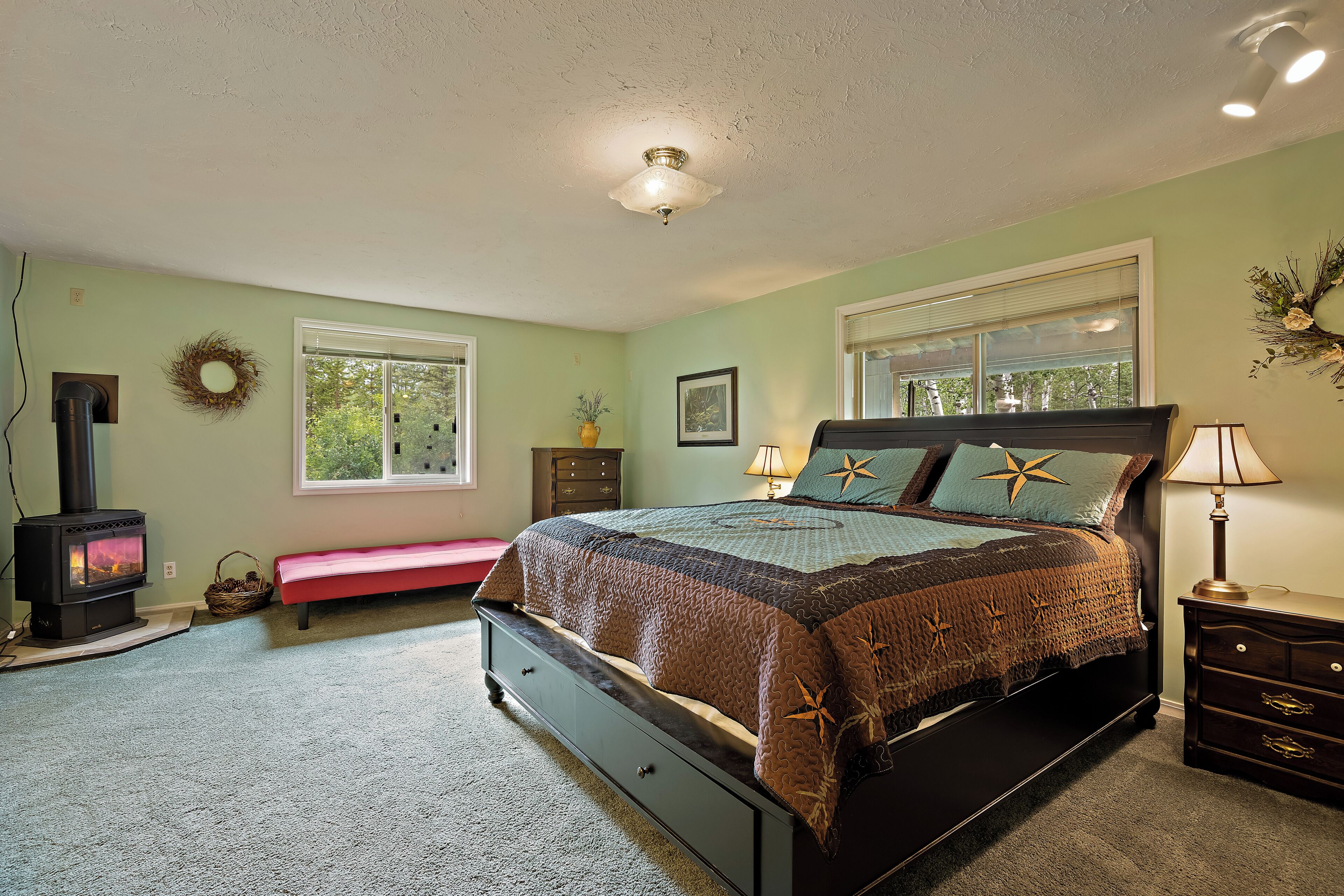 A bedroom with a bed, a dresser, a bench, a fireplace, and a window.