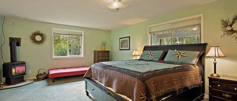 A bedroom with a bed, a dresser, a bench, a fireplace, and a window.