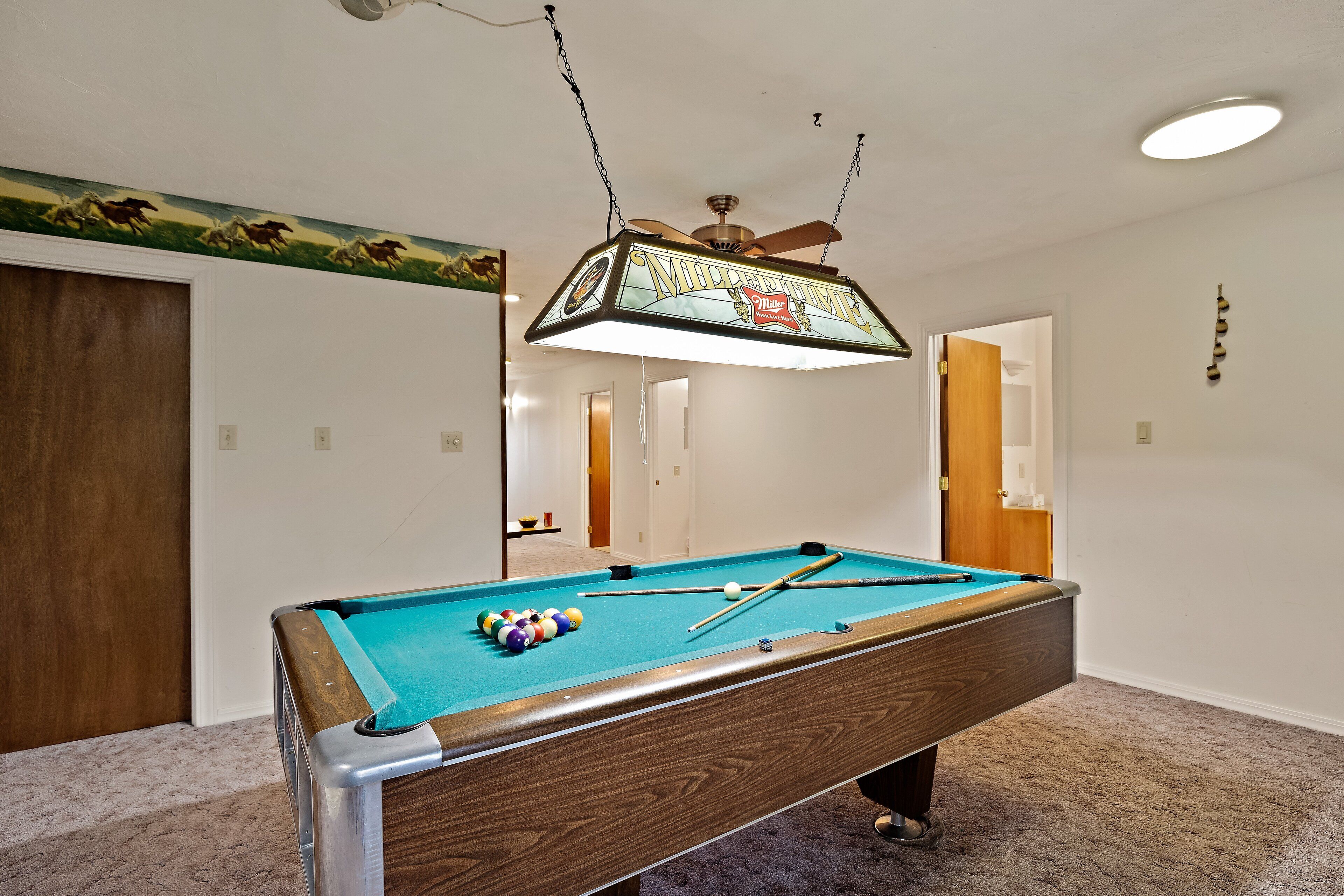 A pool table with a wooden frame and a green felt surface, a ceiling fan, and a wall-mounted light fixture.