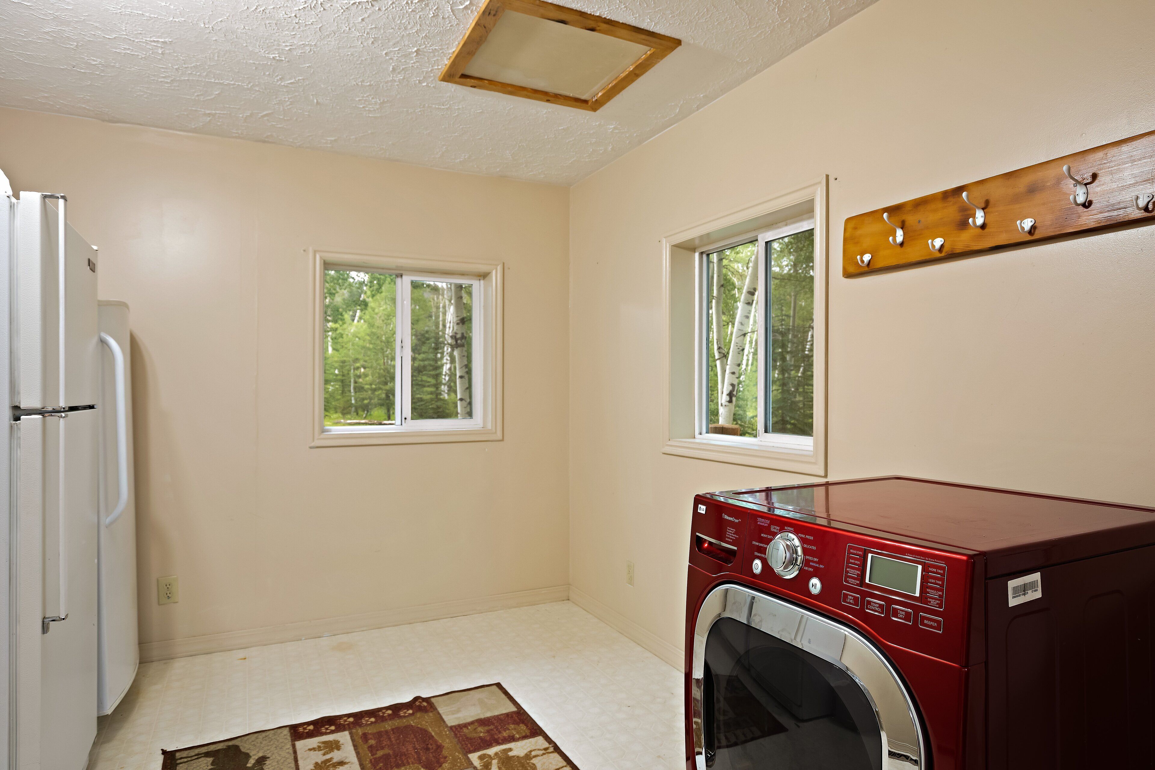 A laundry room with a red washer and dryer, two windows, and a wooden coat rack.