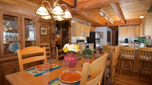 A wooden dining area with a table set for four, surrounded by wooden chairs. A chandelier hangs above the table, and there are glass cabinets with decorative items on the left. - Grand View Retreat (Island Park)