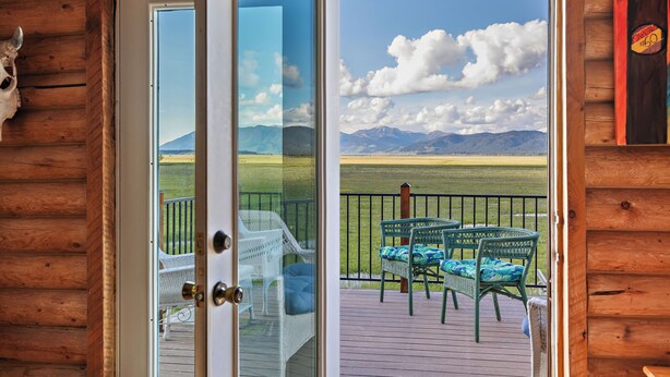 A wooden cabin with a glass door leading to a deck with wicker furniture and a view of mountains. - Grand View Retreat (Island Park)