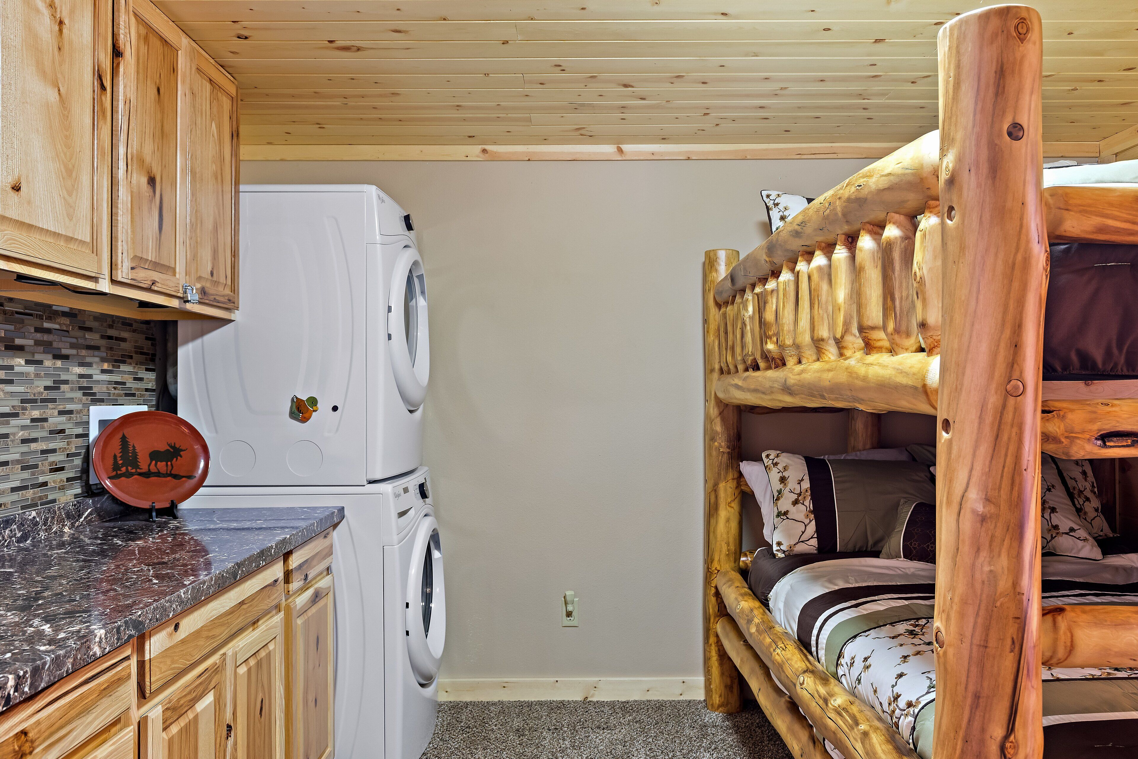Habitación compacta con lavadora, cama con cabecera de madera y zona de cocina con armarios de madera y encimera de mármol.