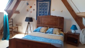 Un dormitori amb un llit de fusta, una tauleta de nit amb una làmpada, una cadira i una finestra amb cortines.