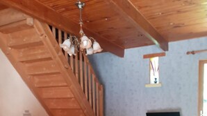 Una habitació acollidora amb una escala de fusta, una televisió sobre un suport de fusta i un sofà amb una funda groga.