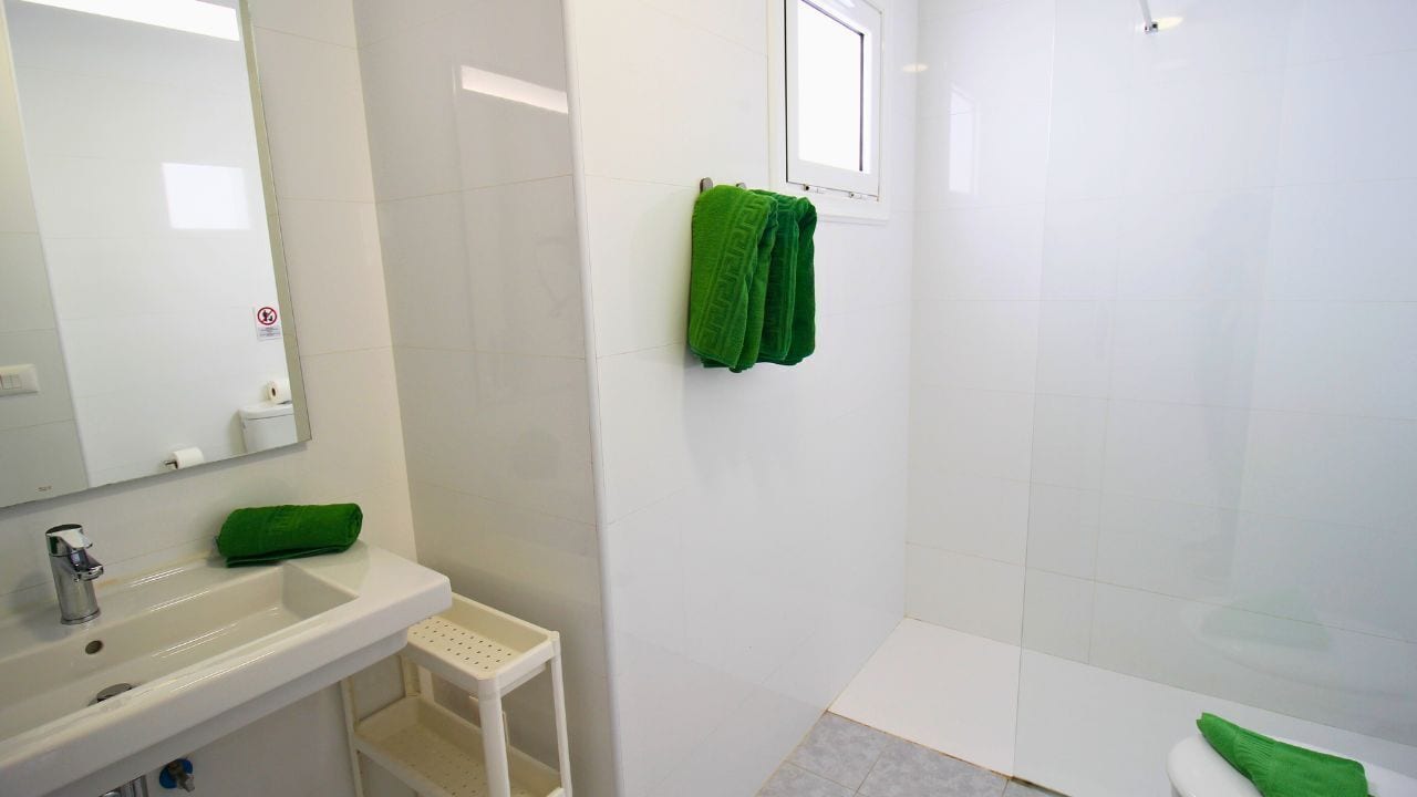 Een badkamer met een wit wastafelmeubel, spiegel en groene handdoeken.