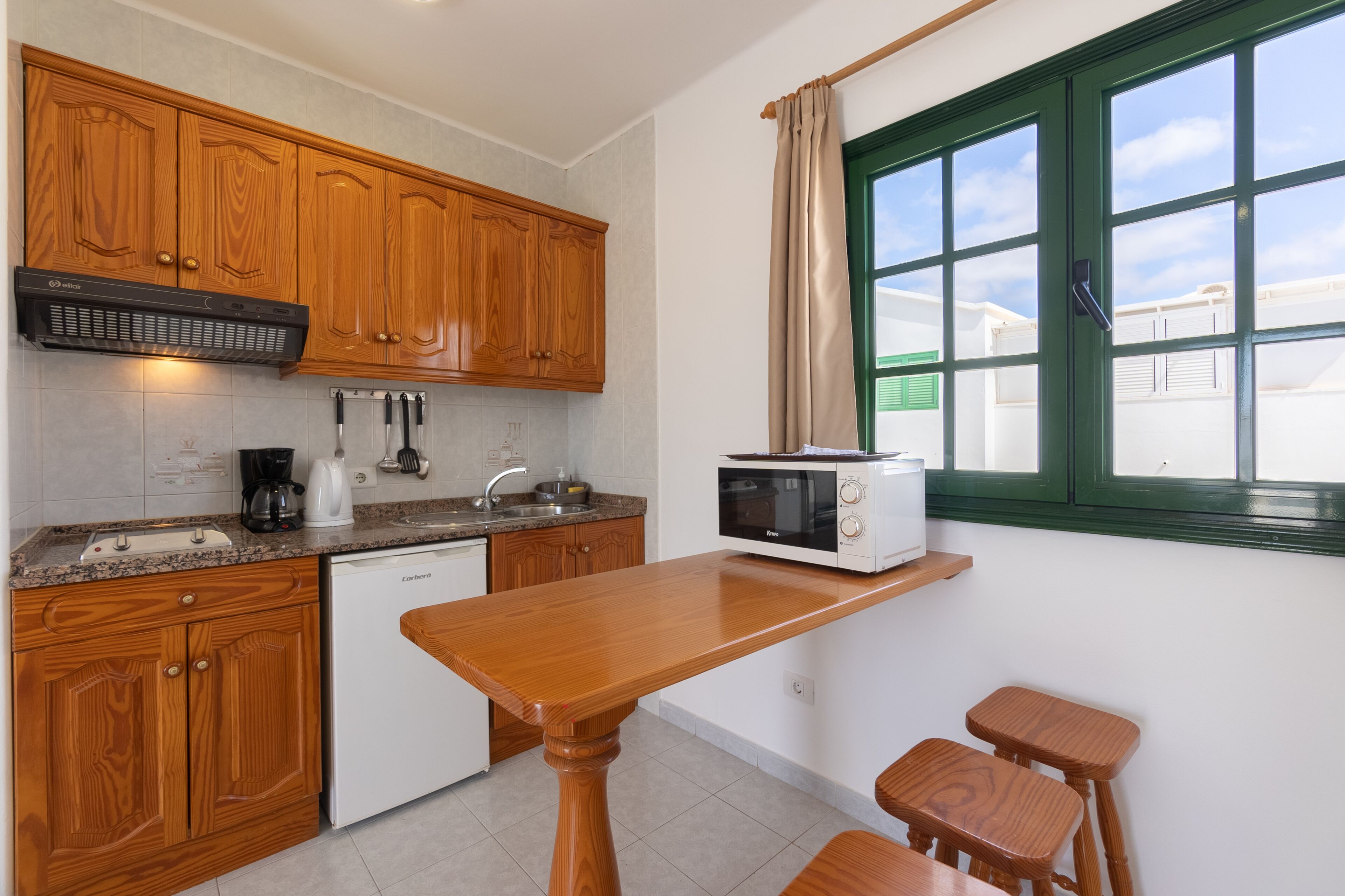 A kitchen with wooden cabinets, a microwave, a coffee maker, and a sink.