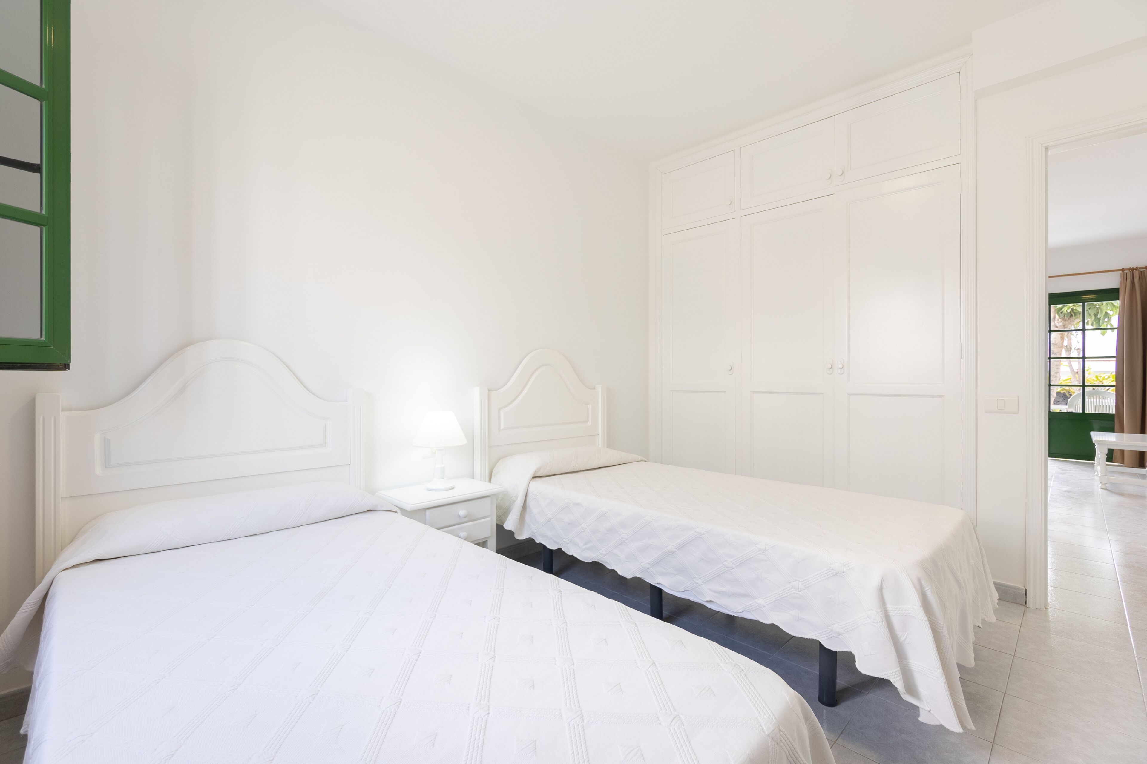 A room with two single beds, a nightstand with a lamp, and a large white wardrobe.