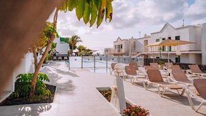 A poolside area with lounge chairs, a swimming pool, and a building with a balcony.