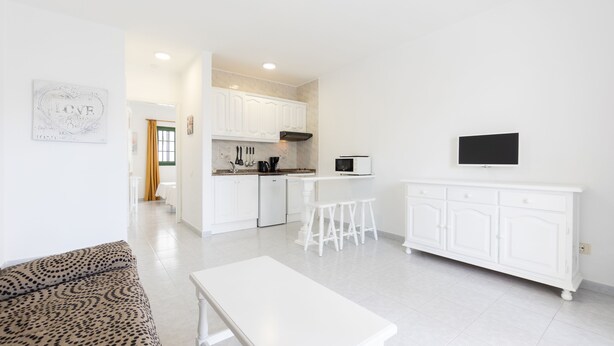 Una cocina moderna con armarios blancos, un comedor con mesa y sillas blancas, y un sofá con estampado de leopardo.