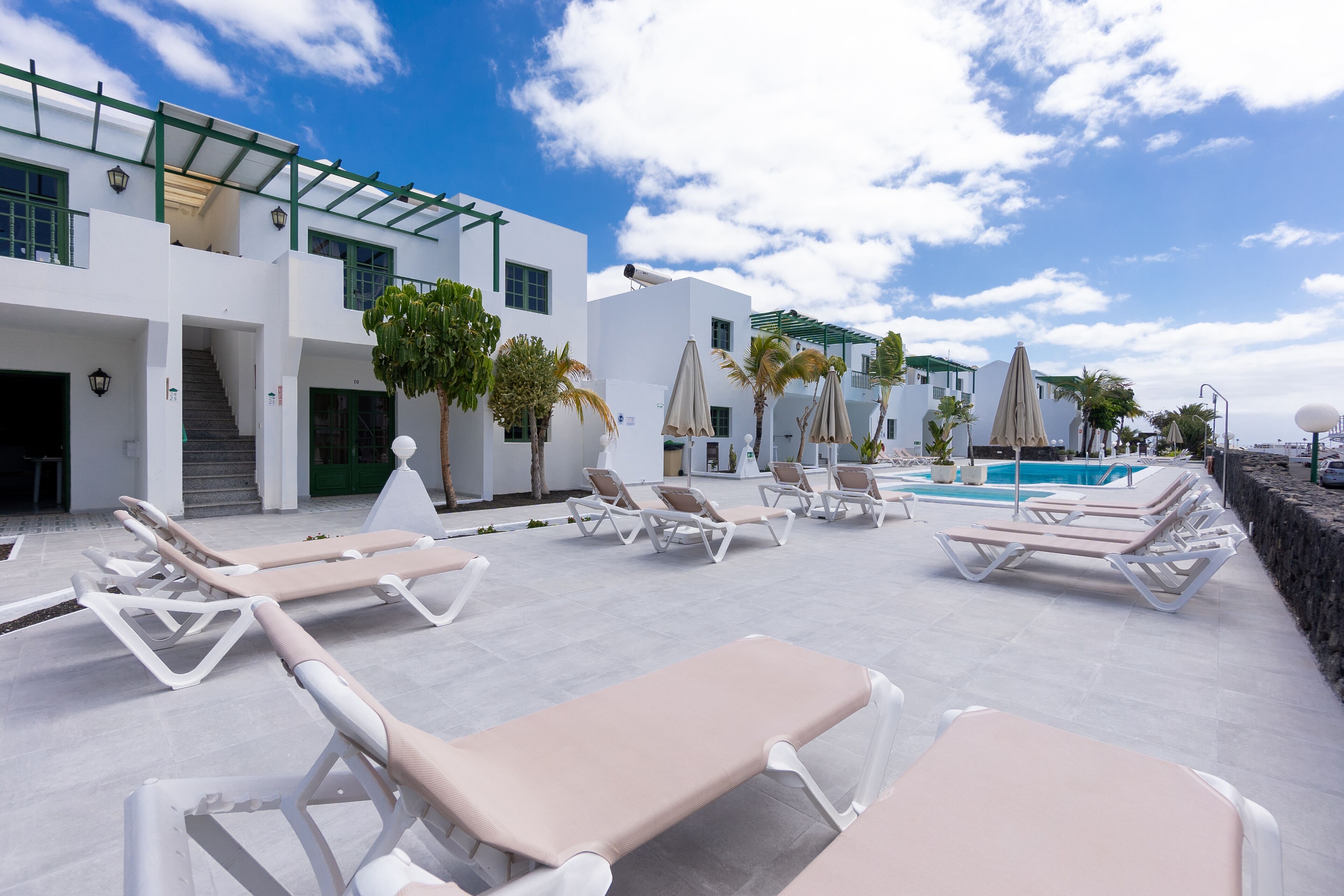 Un área de piscina en la azotea con tumbonas, una piscina y un edificio moderno con techo verde.