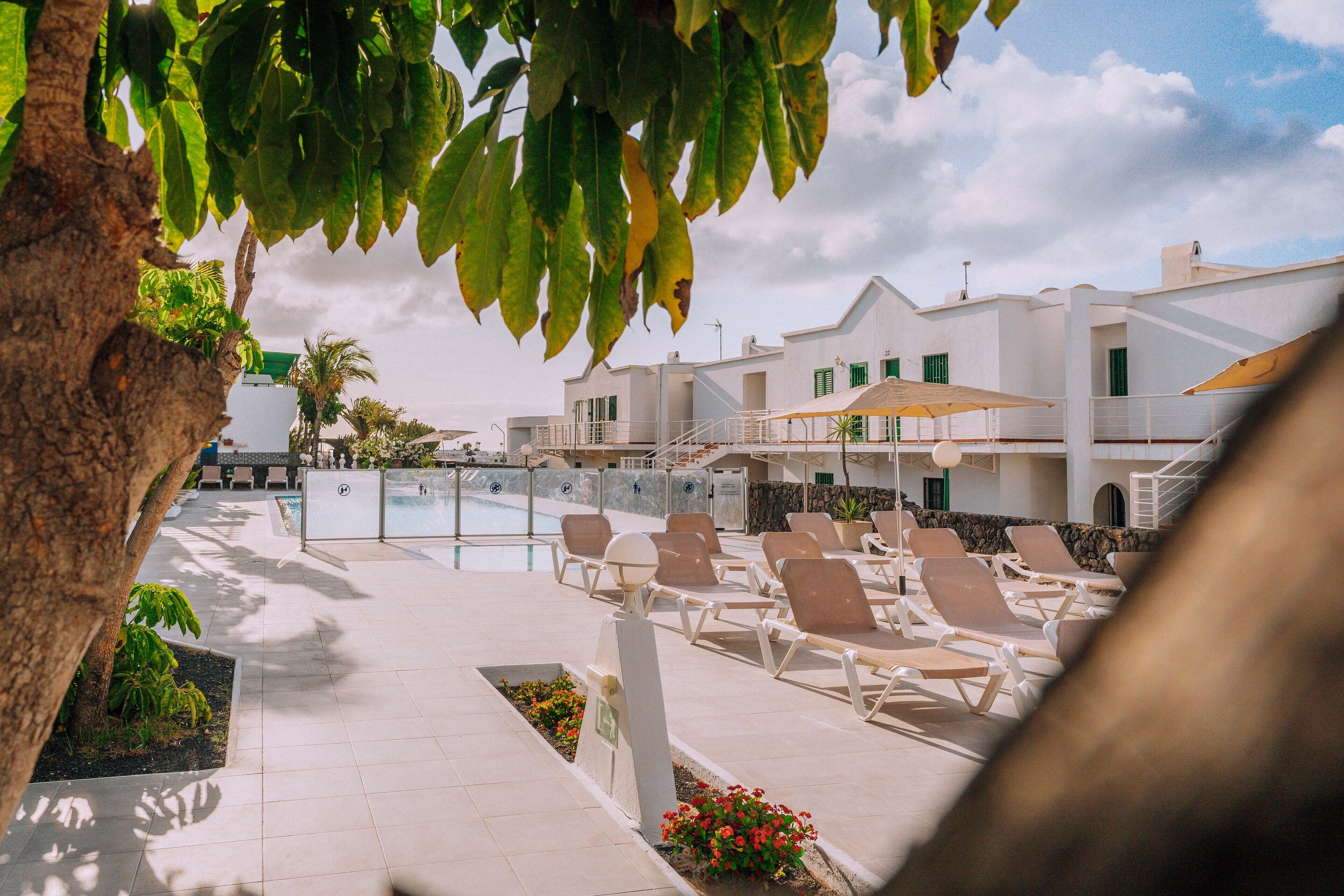 Un espace aménagé au bord de la piscine, avec des chaises longues, une piscine et un bâtiment aux murs blancs et aux volets verts.
