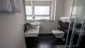 Un baño moderno con un lavamanos blanco, inodoro y cabina de ducha con mampara de cristal.