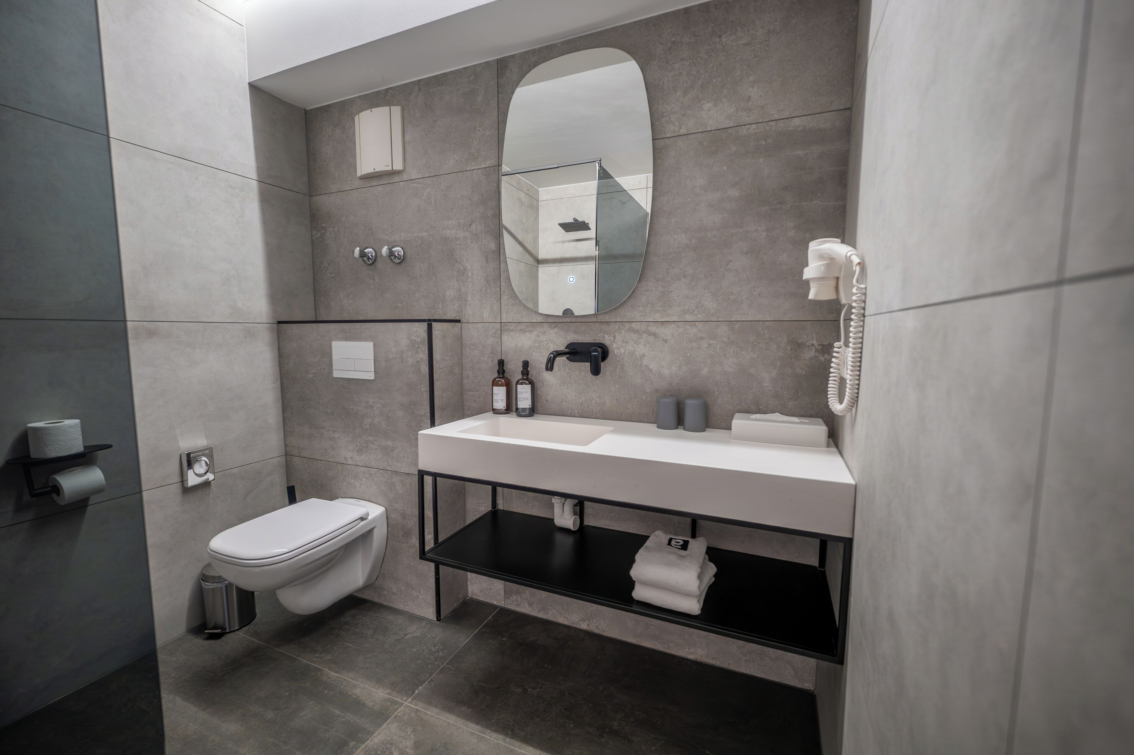 A modern bathroom with a toilet, sink, mirror, and a telephone.