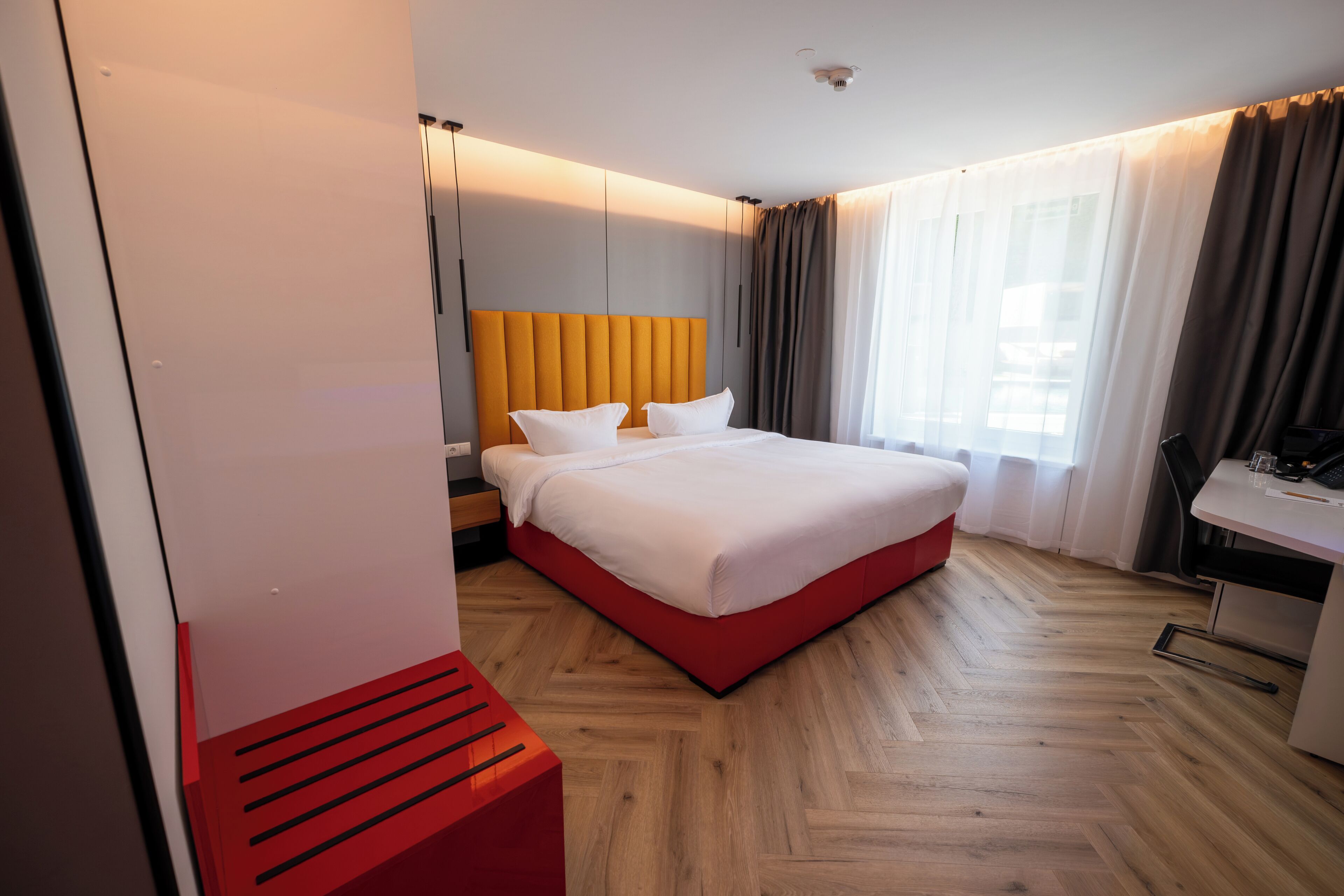 A hotel room with a bed, a desk, a chair, and a window with curtains.