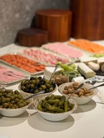 A buffet table with various food items including olives, pickles, and meats.