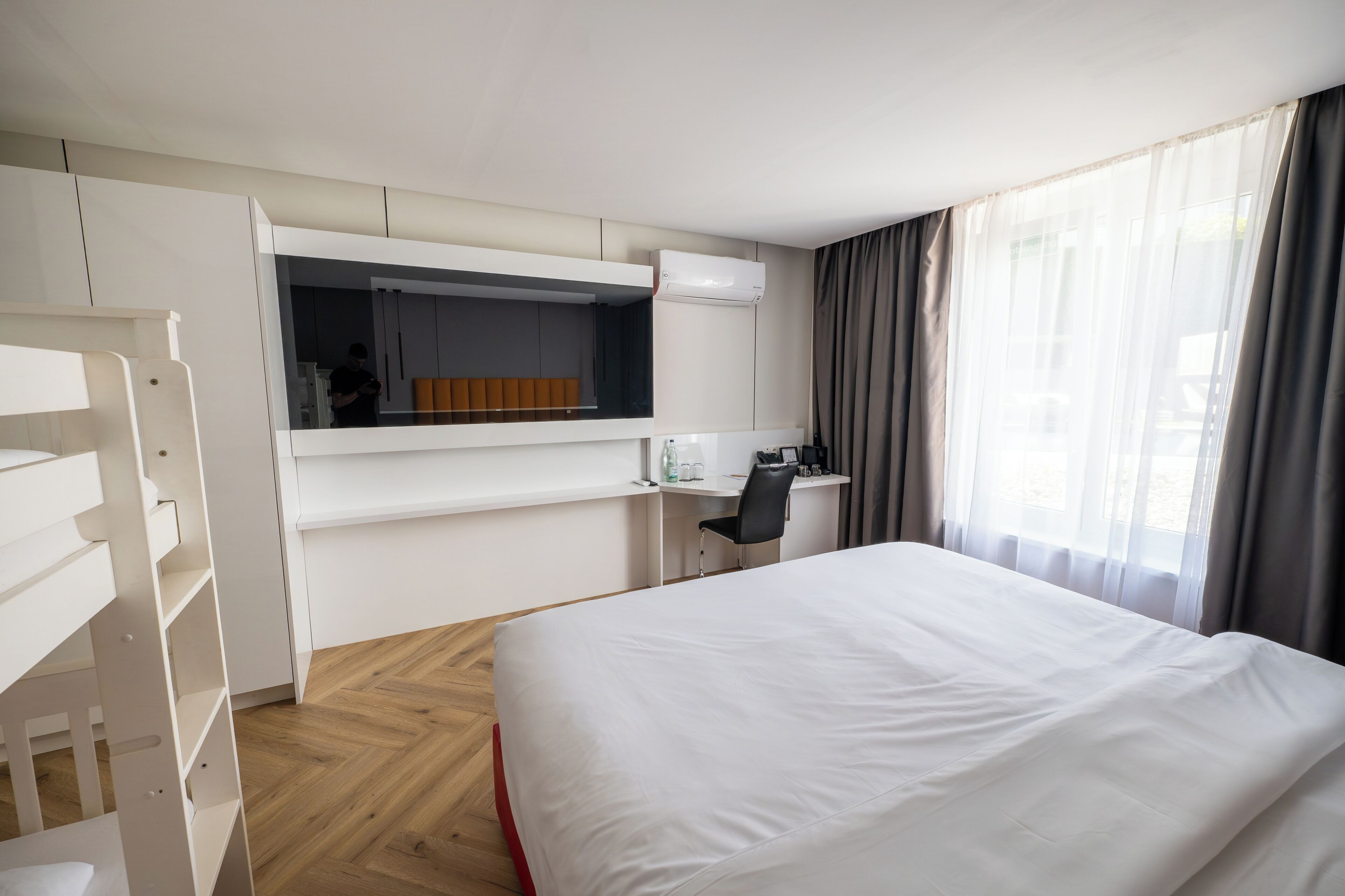 A hotel room with a bed, a desk, a chair, a wardrobe, and a window with curtains.