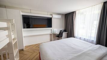 A hotel room with a bed, a desk, a chair, a wardrobe, and a window with curtains.