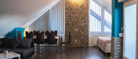 A modern living room with a dining area, a stone accent wall, and a view of a staircase.