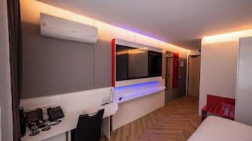 Une chambre d’hôtel avec un lit, un bureau avec un téléphone, un miroir, un climatiseur et un banc rouge.