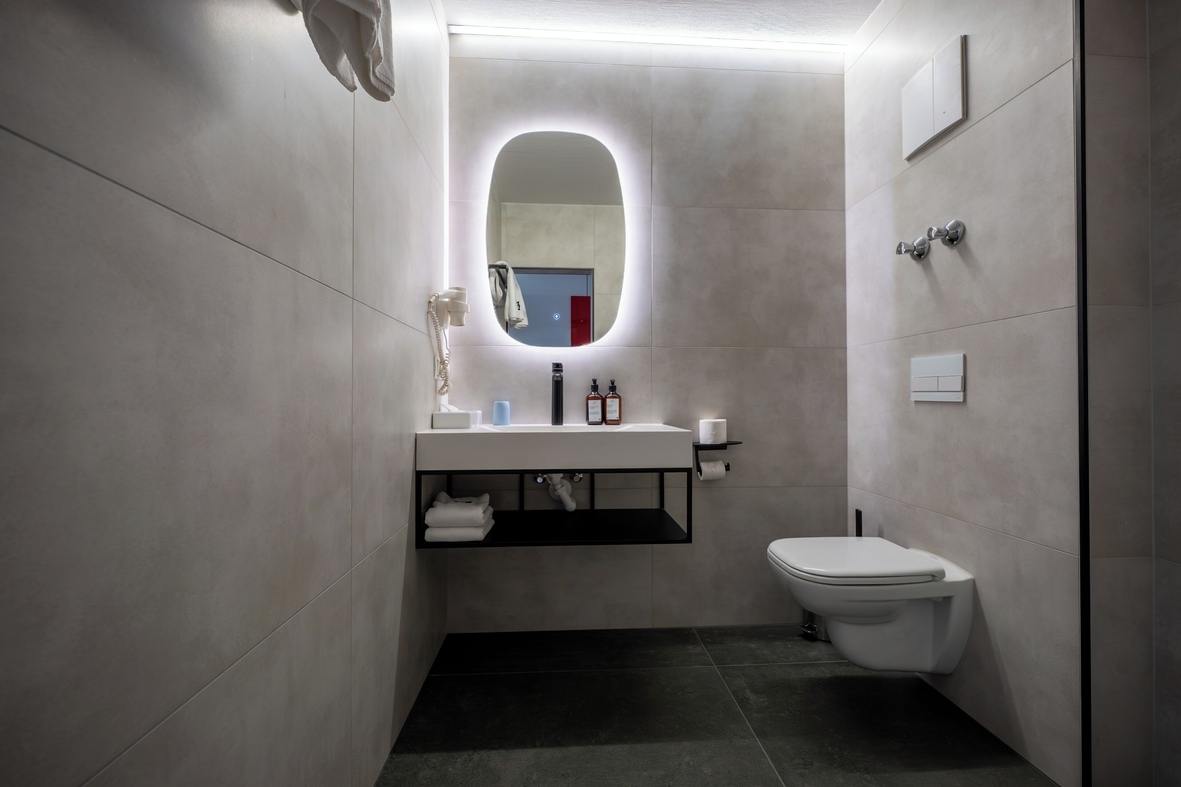 A modern bathroom with a white sink, a mirror, a toilet, and a towel rack.