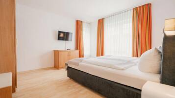 A modern hotel room with a large bed, wooden wardrobe, and a flat-screen TV on the wall.