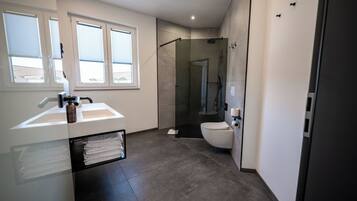 Een moderne badkamer met een douchecabine van glas, een wit wastafelmeubel en een toilet.