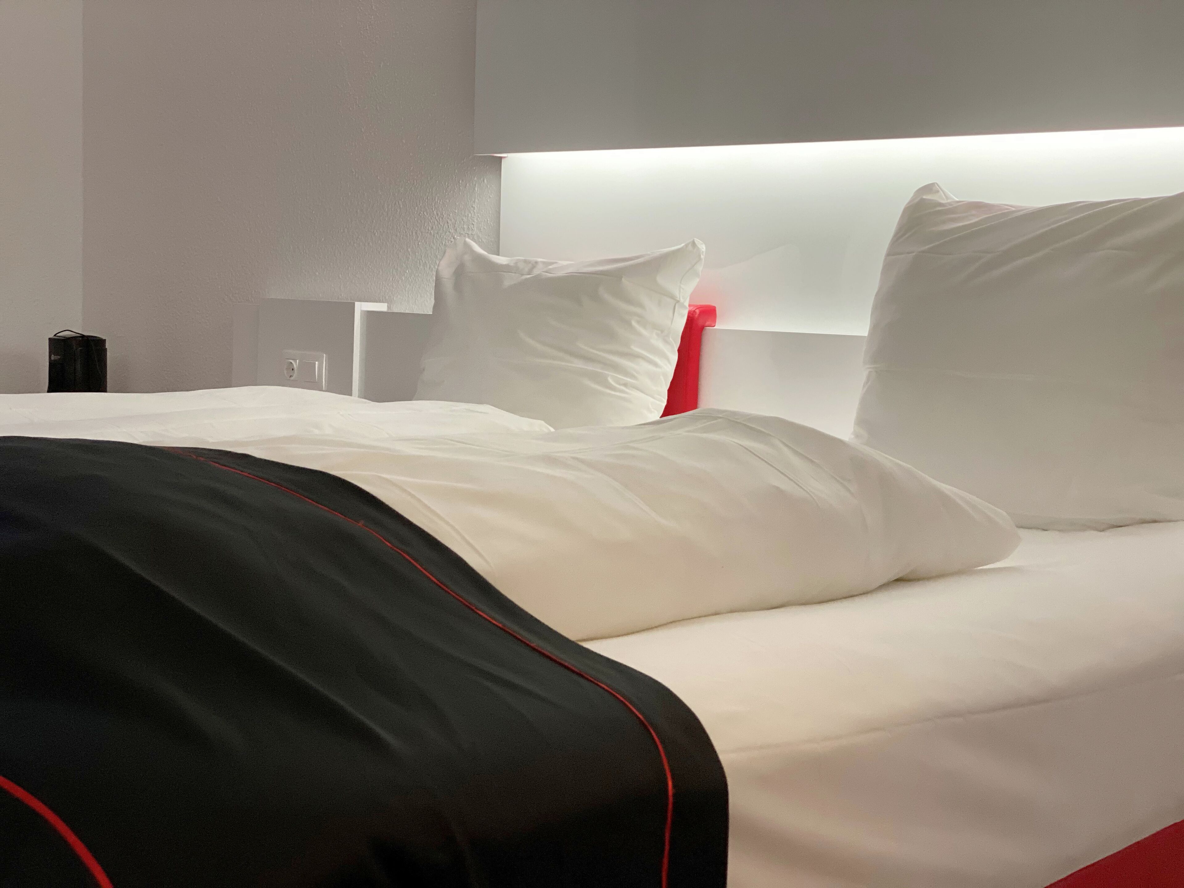 A neatly made bed with white bedding and a black and red striped blanket.
