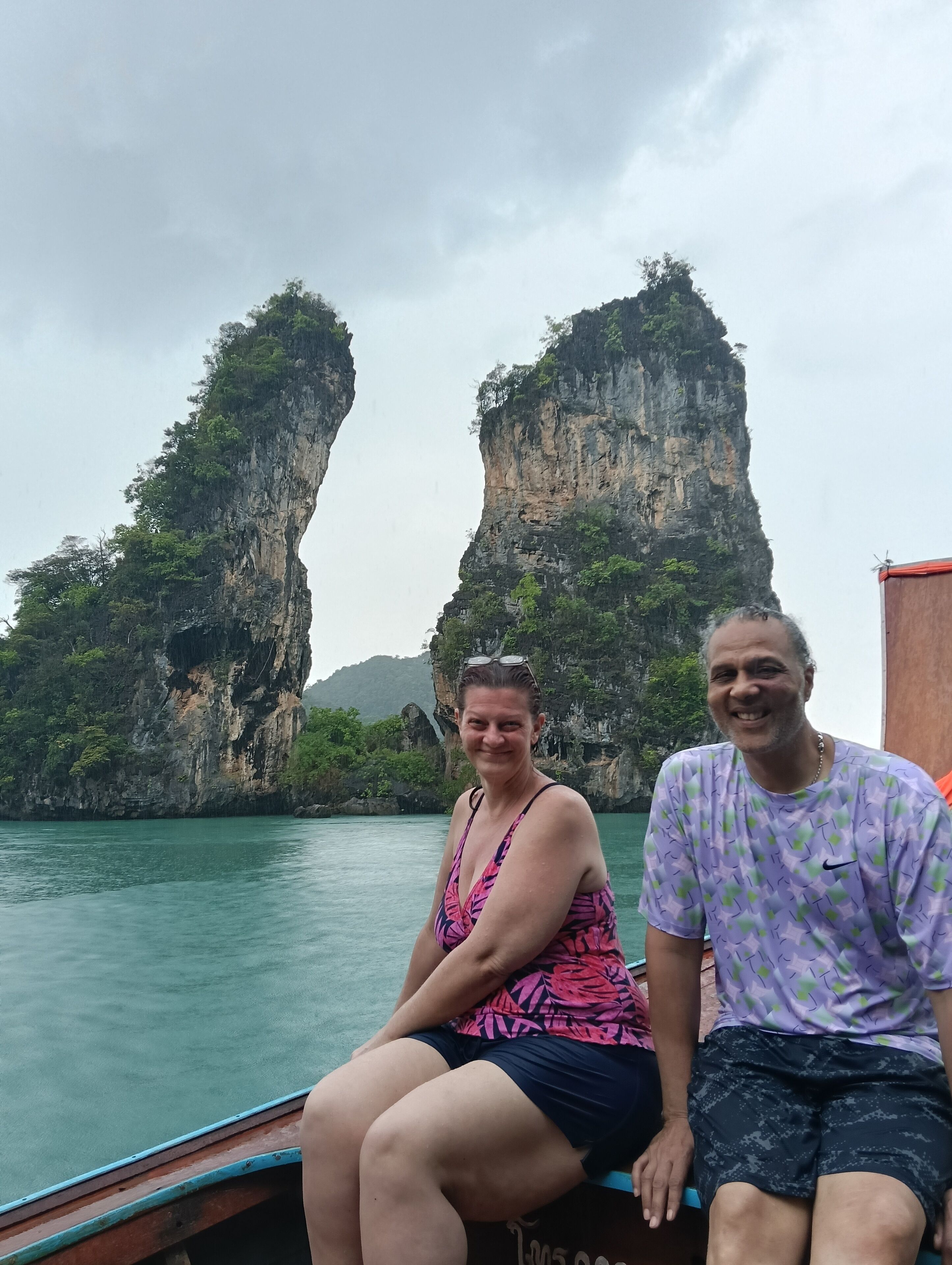 Two people on a boat with a view of tall cliffs and water.