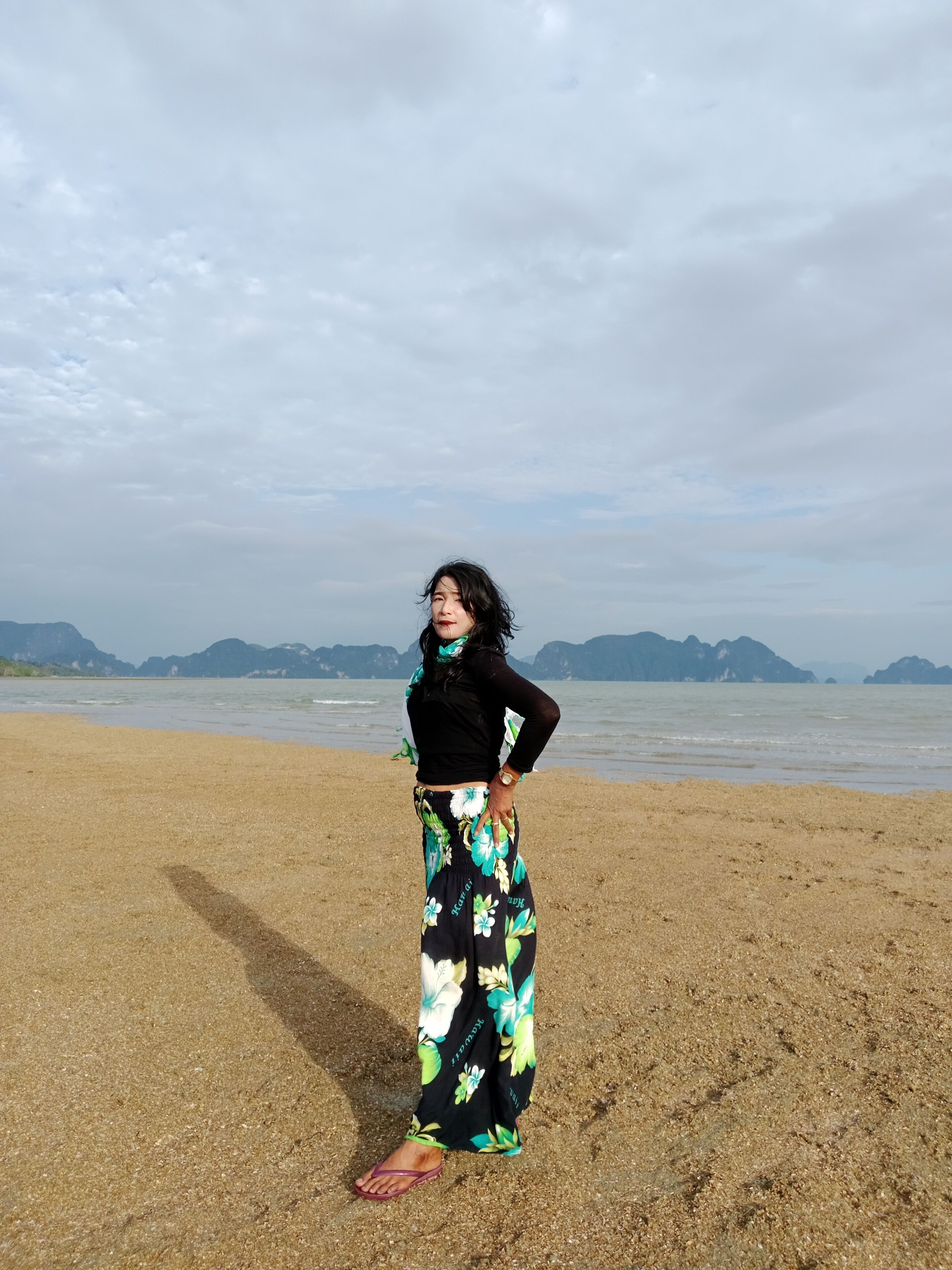 A person standing on a sandy beach with a body of water and distant mountains in the background.