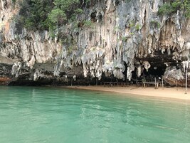 Formación natural de cueva con estalactitas y estalagmitas, una playa de arena y aguas turquesas cristalinas.