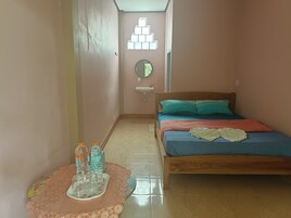 Un estrecho pasillo que conduce a un dormitorio con una cama, una mesita de noche con botellas de agua y un espejo montado en la pared.