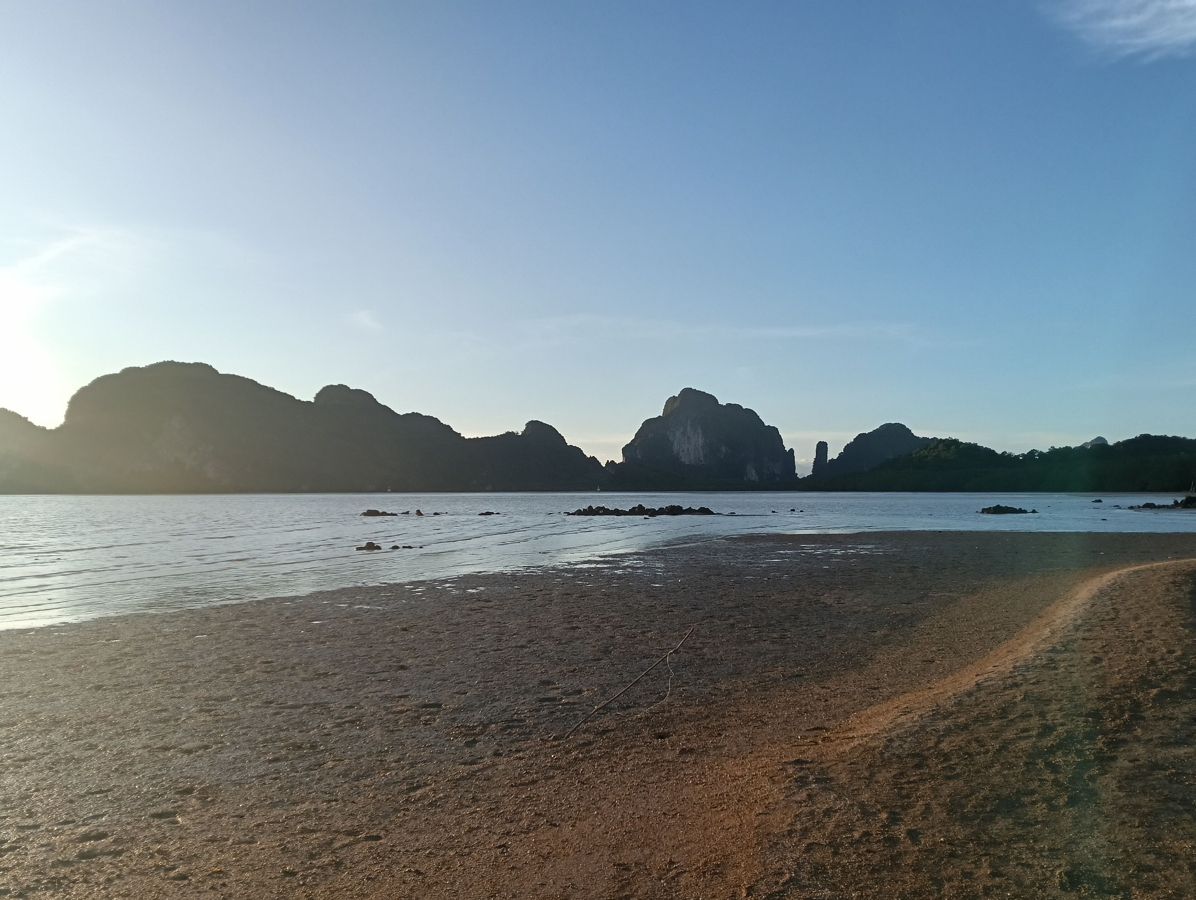 Una playa con terreno rocoso y montañas a lo lejos.