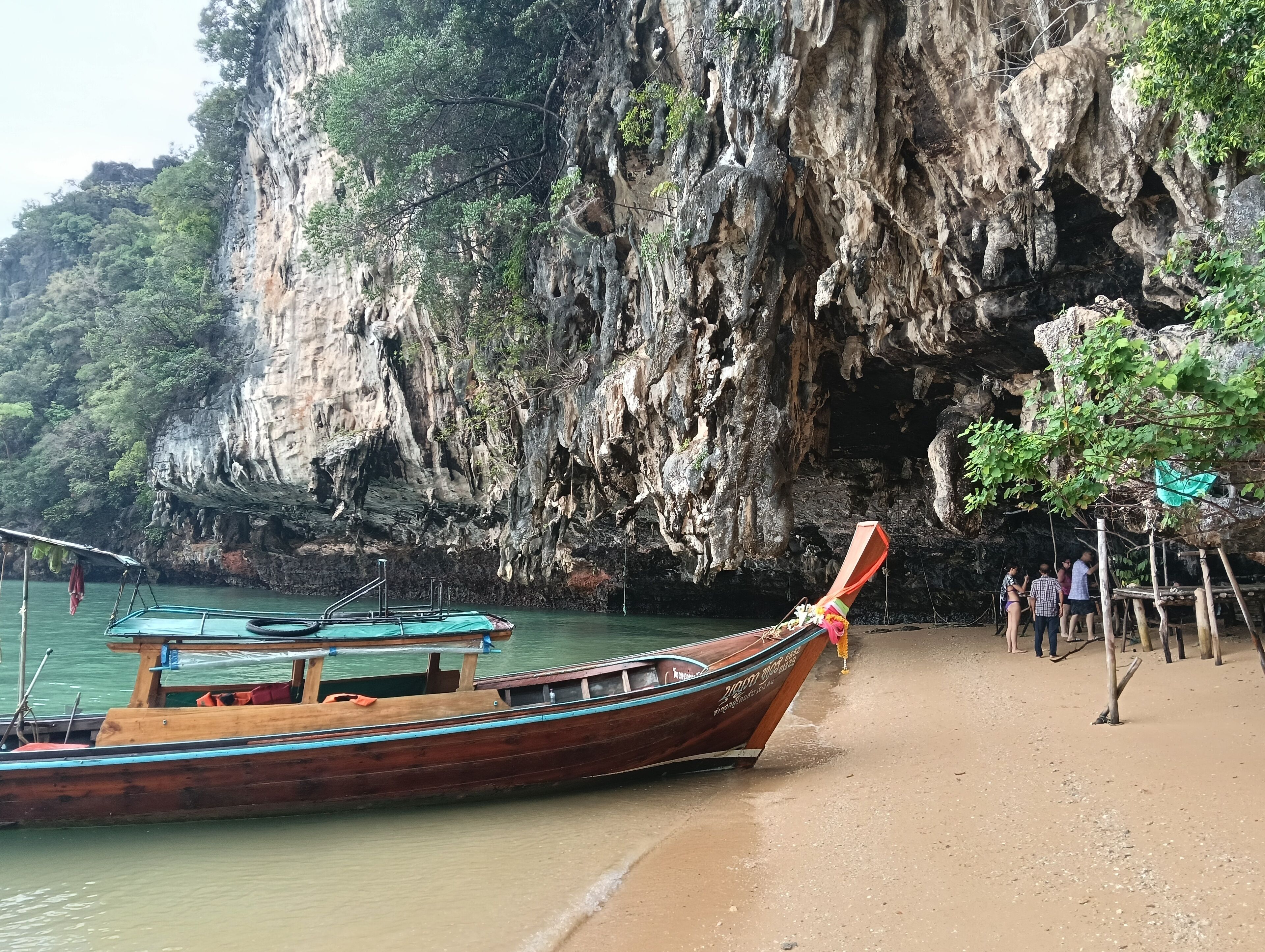 A traditional wooden boat docked at a beach with a rocky cliff in the background.