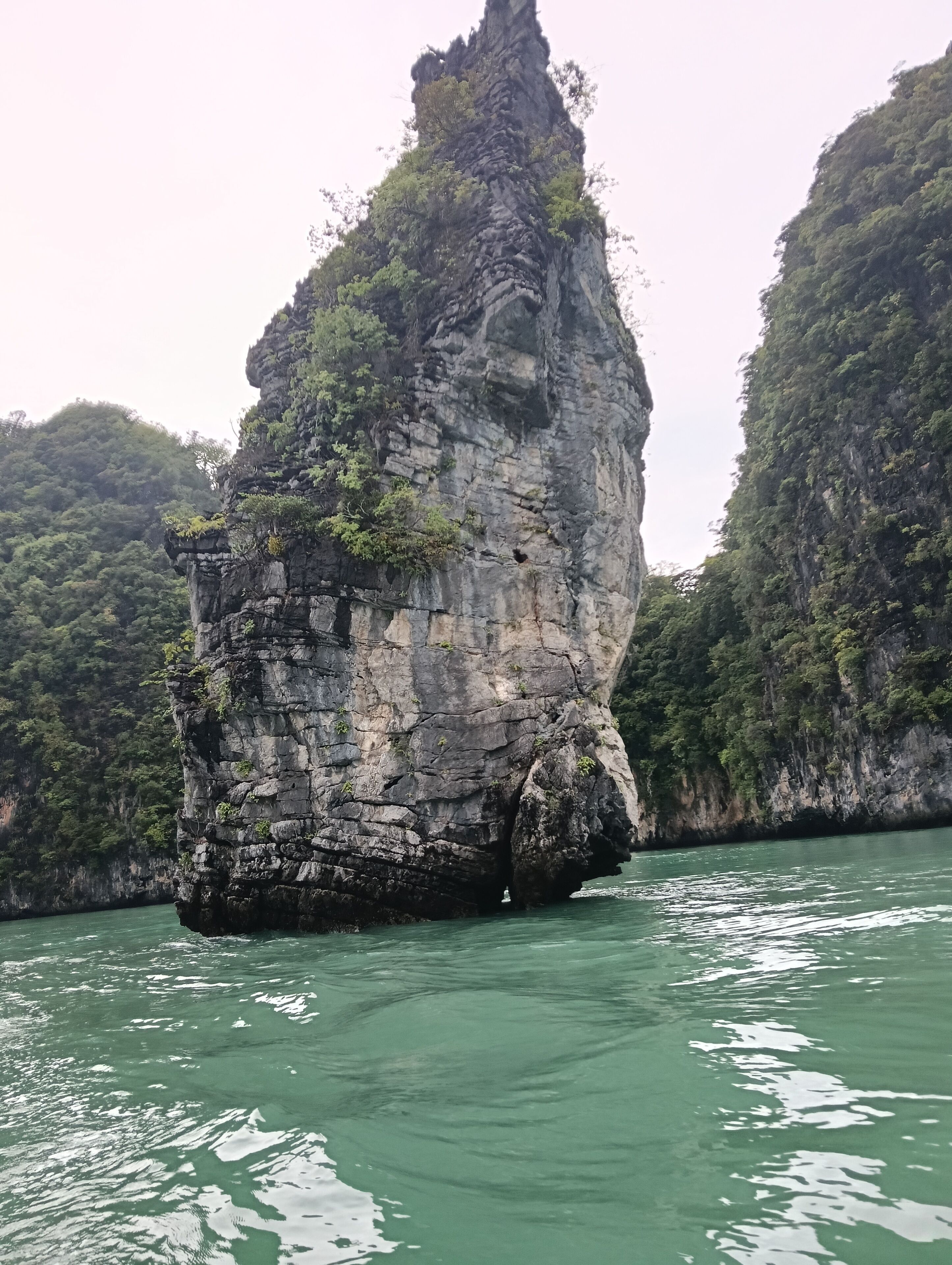 A large rock formation surrounded by water and dense greenery.