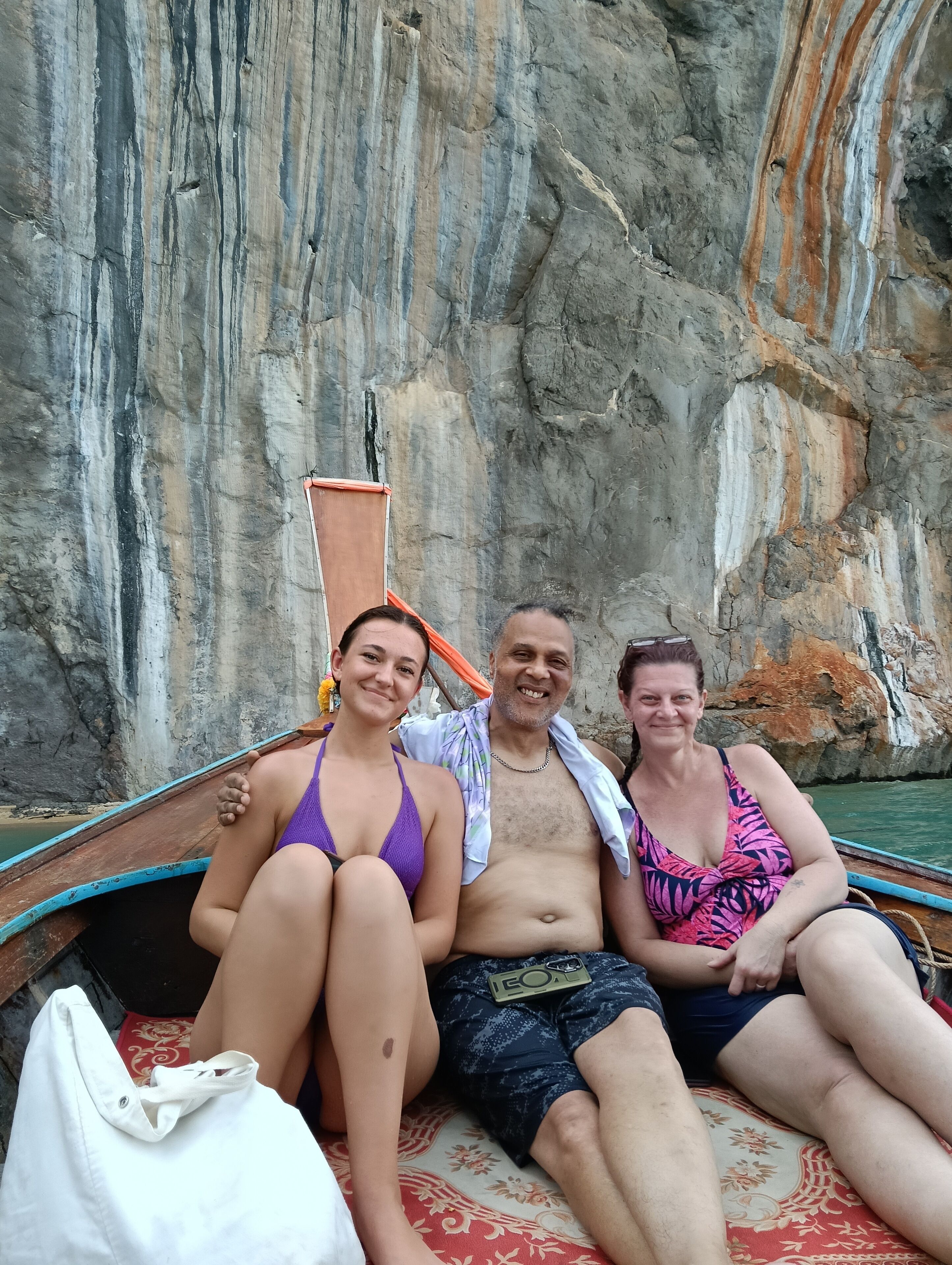 Three people seated on a boat with a rocky cliff in the background.