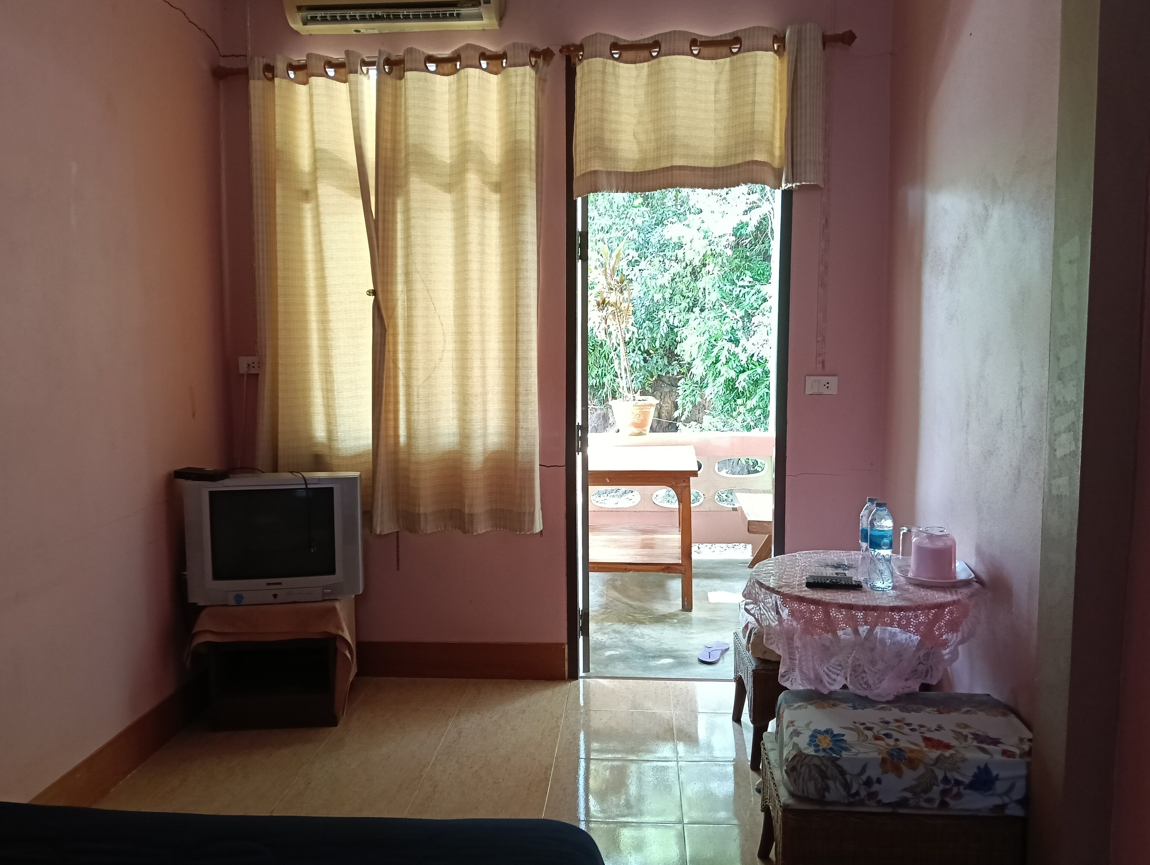 A room with a television on a wooden stand, a small table with a lace tablecloth, and a bed with a floral bedspread.