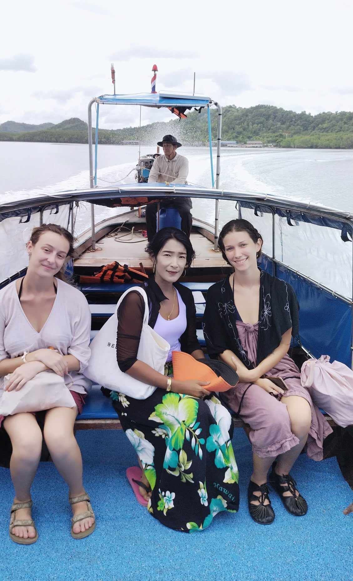 Three people seated on a boat with a view of a body of water and hills in the background.