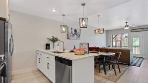 A modern kitchen with a built-in dishwasher, a dining area with a bench, pendant lights, and a 'WELCOME' sign. - Alluring Farmhouse Styled Town Home (McCall)