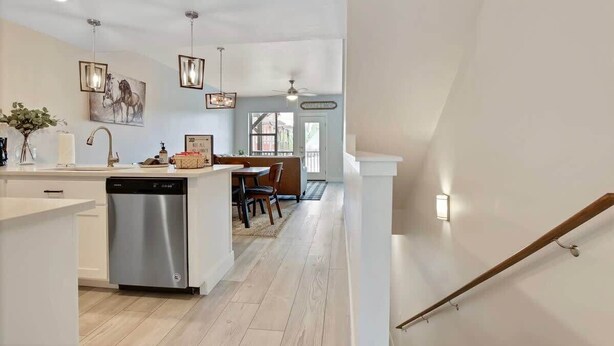 A modern kitchen with a dishwasher, a dining area with a table and chairs, and a staircase leading to another level. - Alluring Farmhouse Styled Town Home (McCall)