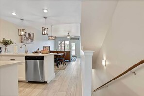 A modern kitchen with a dishwasher, a dining area with a table and chairs, and a staircase leading to another level. - Alluring Farmhouse Styled Town Home (McCall)