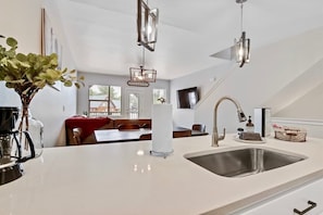 Una cocina moderna con una isla grande, pileta de acero inoxidable e iluminación colgante.