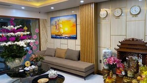 Een moderne woonkamer met een bank, een salontafel, een schilderij van een schip en klokken die de tijd in Tokio, Seoul en Hanoi weergeven.