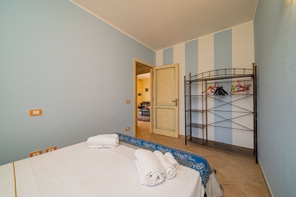 A hotel room with a bed, a metal drying rack, and a door leading to another room.