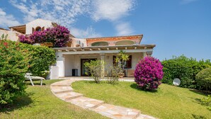 A Mediterranean-style villa with a stone pathway leading to the entrance, surrounded by lush greenery and flowering plants. - Casa Hermes (Olbia)