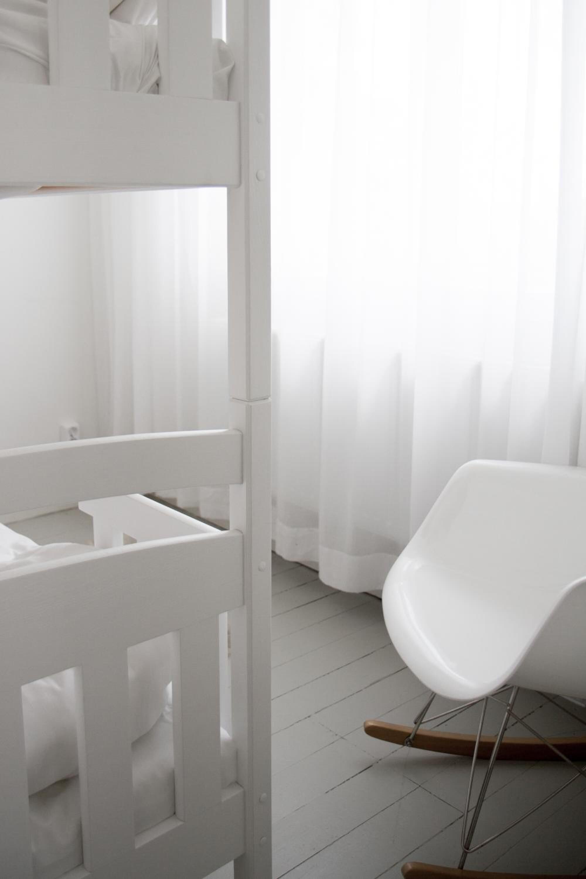 Una mecedora blanca en una habitación con un armario blanco y una cortina translúcida.