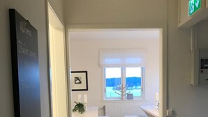 A hallway leading to a dining area with white benches and a table, a framed picture on the wall, and a view of the outdoors through a window.