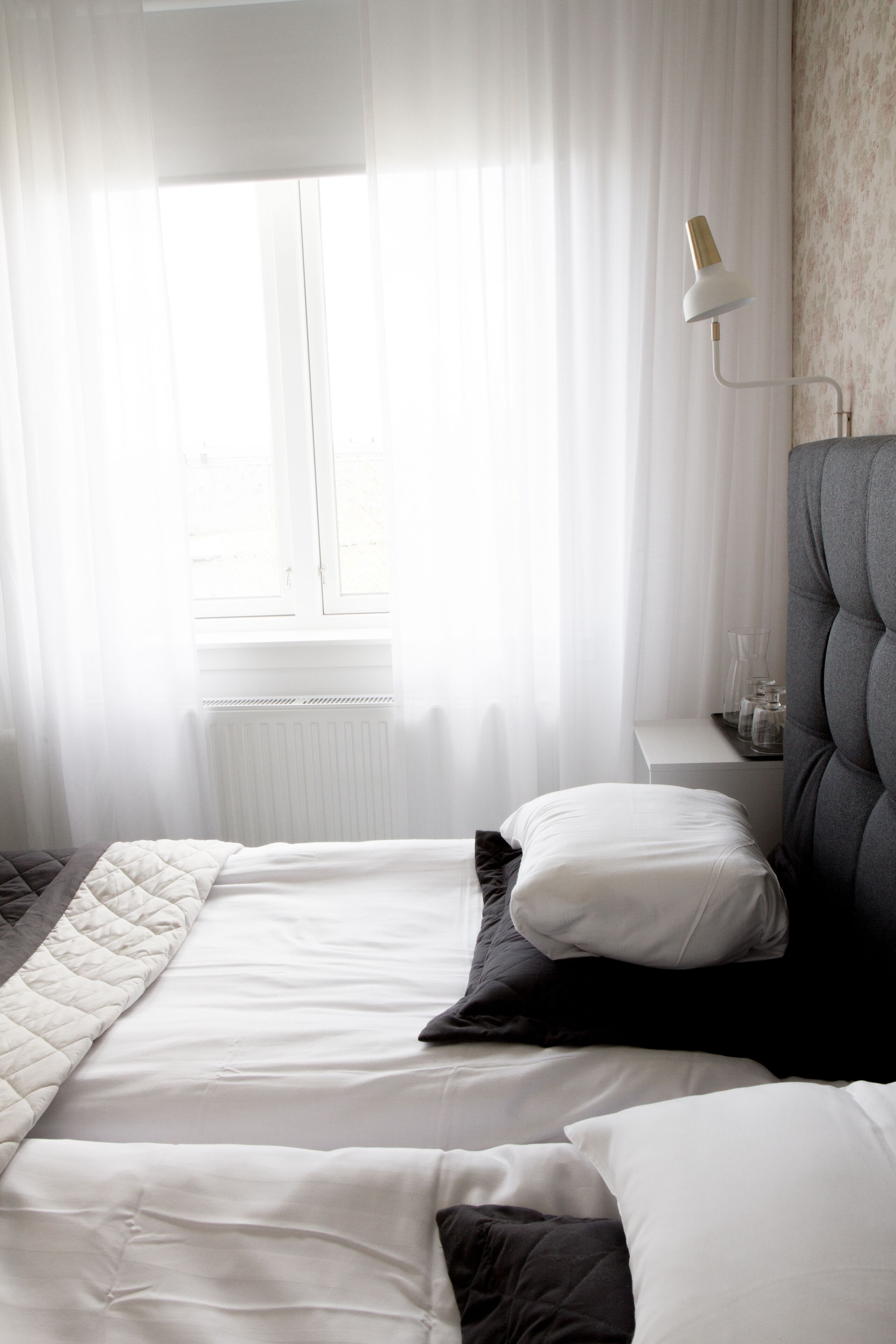 A bedroom with a bed, white curtains, a bedside lamp, and a radiator.